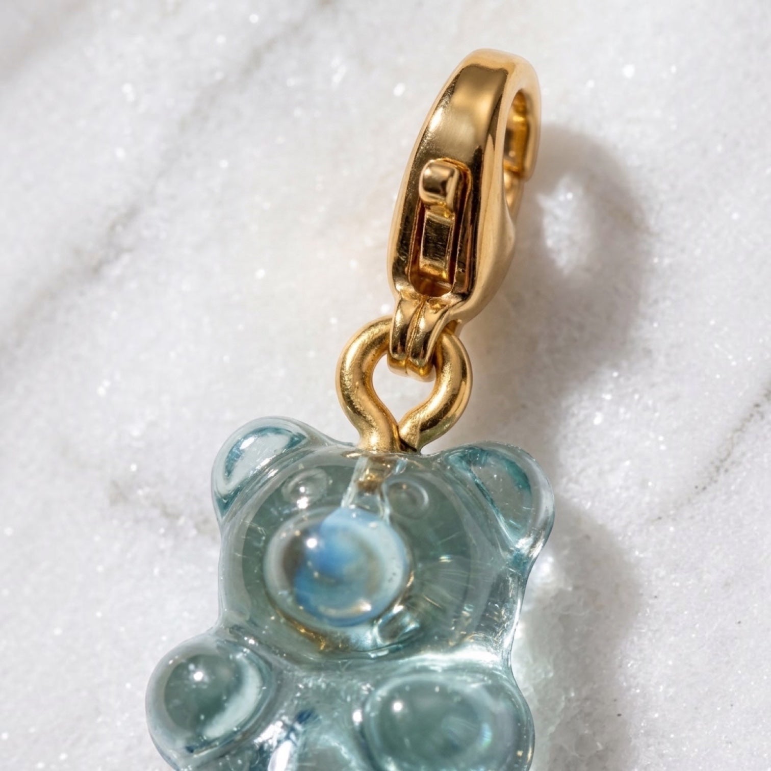 Chévereh translucent blue gummy bear resin charm with a polished 14K gold-plated lobster clasp on marble background