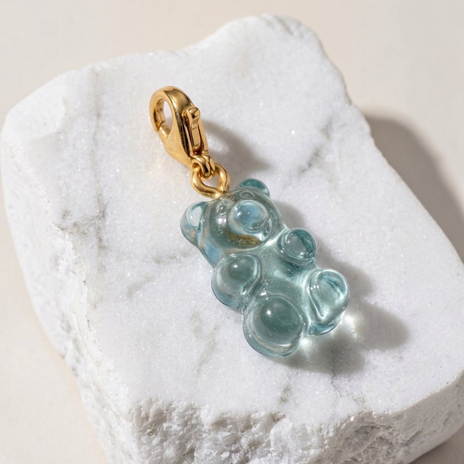 Chévereh translucent blue gummy bear resin charm with a 14K gold-plated lobster clasp on a white marble stone