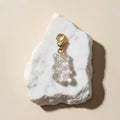 Chévereh clear resin gummy bear charm with a 14K gold-plated lobster clasp resting on a white marble stone.