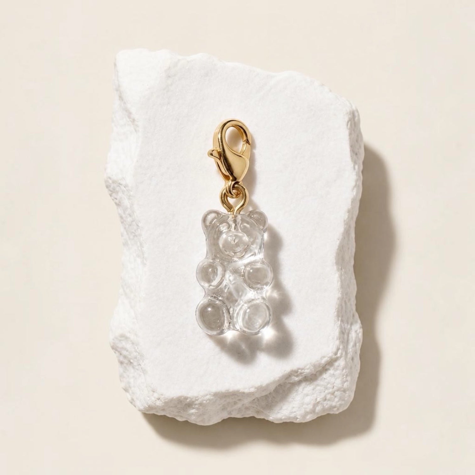 Chévereh clear resin gummy bear charm with a polished 14K gold-plated lobster clasp on a textured white stone base.