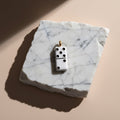 Chévereh white stainless steel domino charm with black dots and gold bail, on marble.