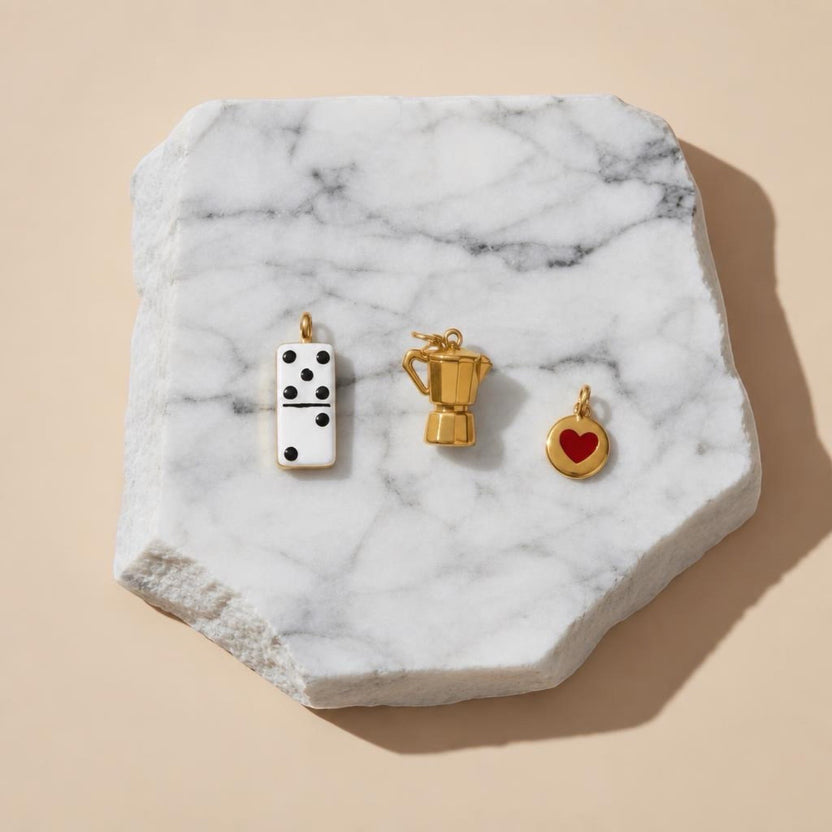 Chévereh gold-plated stainless steel charms: white domino, greca coffee pot, and red heart. Culturally inspired.