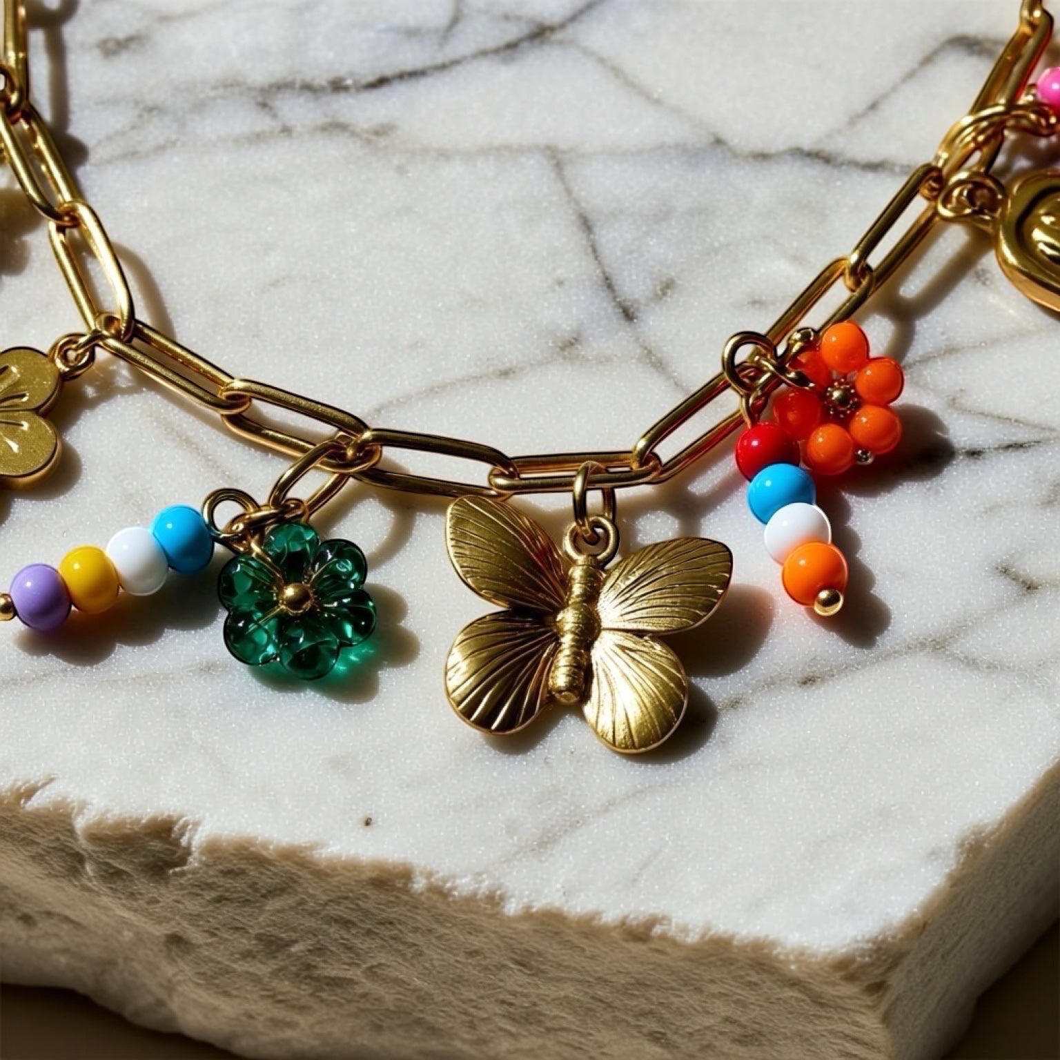 Chévereh gold-tone paperclip chain necklace with butterfly, flower charms, and colorful beaded accents.