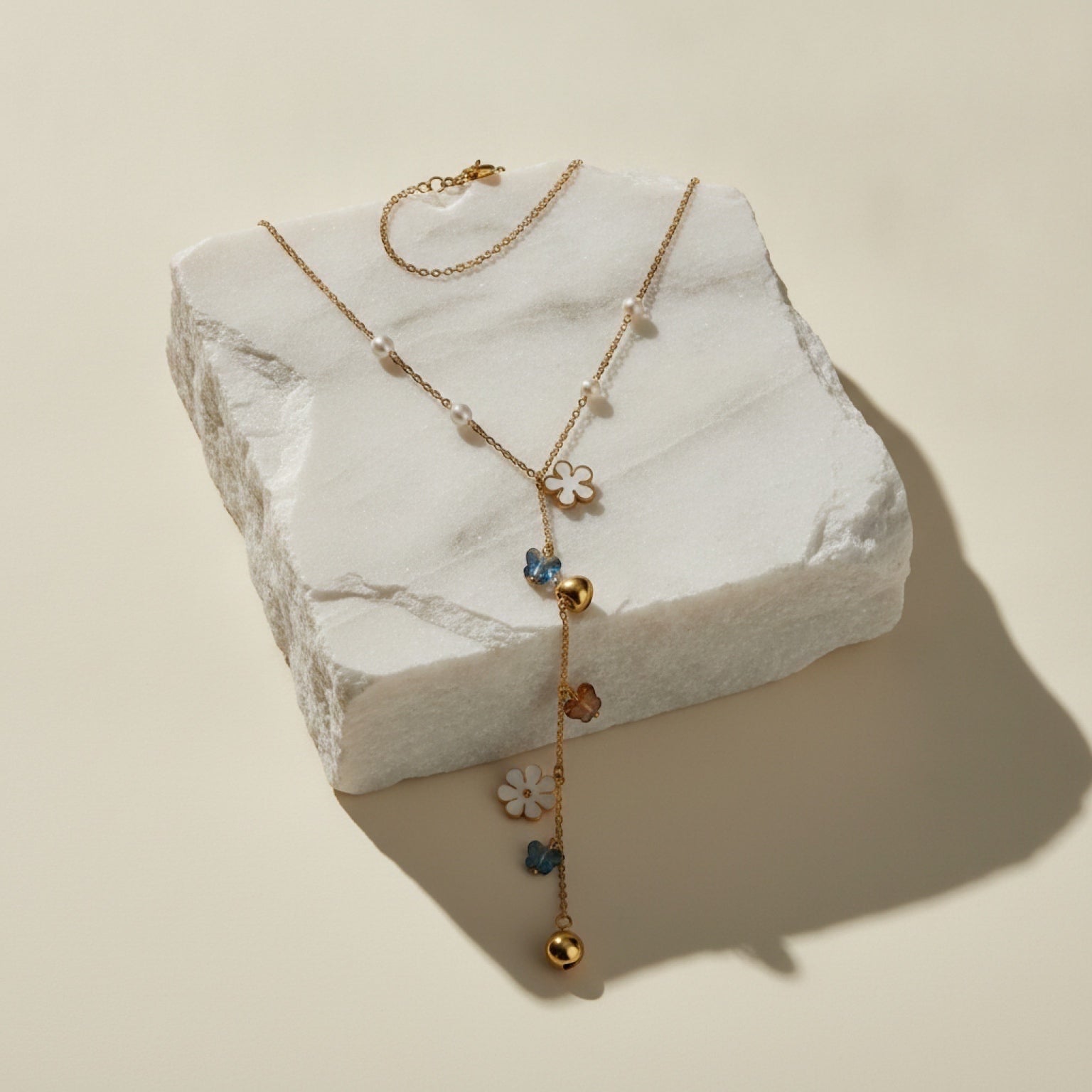 Chévereh gold-tone Y-necklace featuring faux pearls, white flower charms, blue butterflies, and gold heart accents.