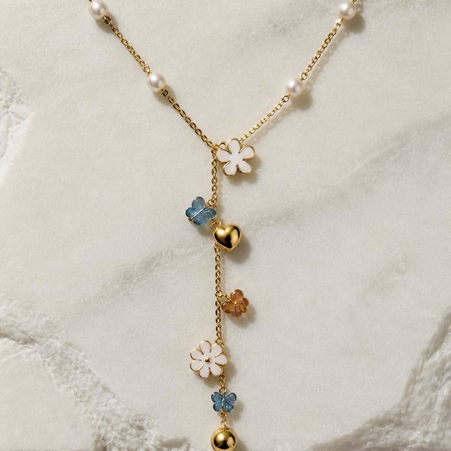 Chévereh gold-tone Y-necklace featuring faux pearls, white flower charms, blue butterfly accents, and gold hearts.