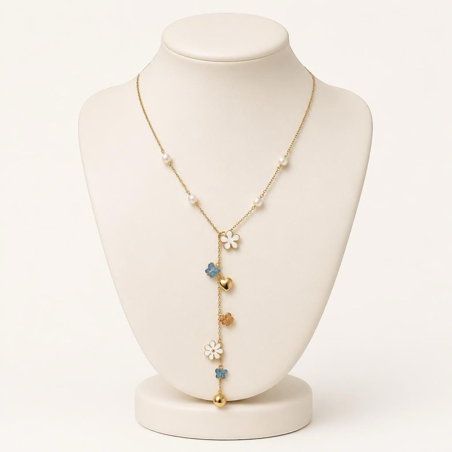 Chévereh gold-tone Y-necklace with faux pearls, white flower charms, blue butterflies, and heart accents on a bust.
