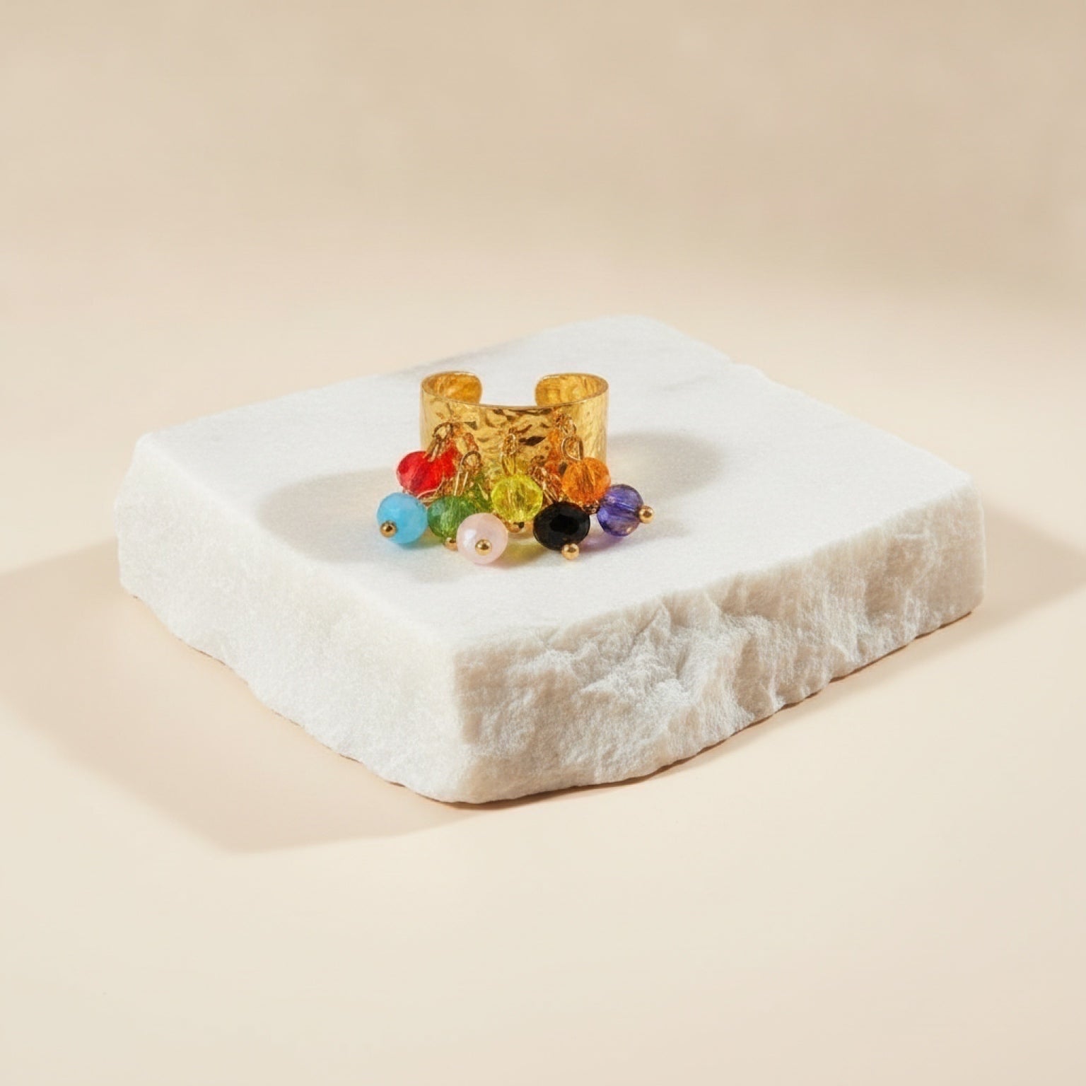 Chévereh gold hammered metal statement ring featuring dangling multi-colored beaded charms on a white stone base.
