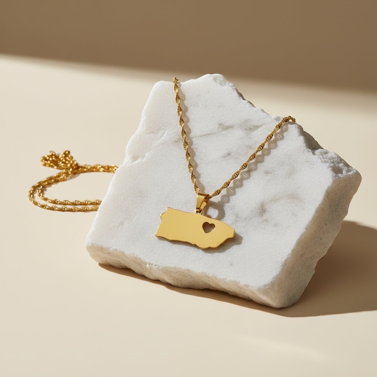 Chévereh gold-tone stainless steel island pendant necklace with heart cutout on a marble surface.