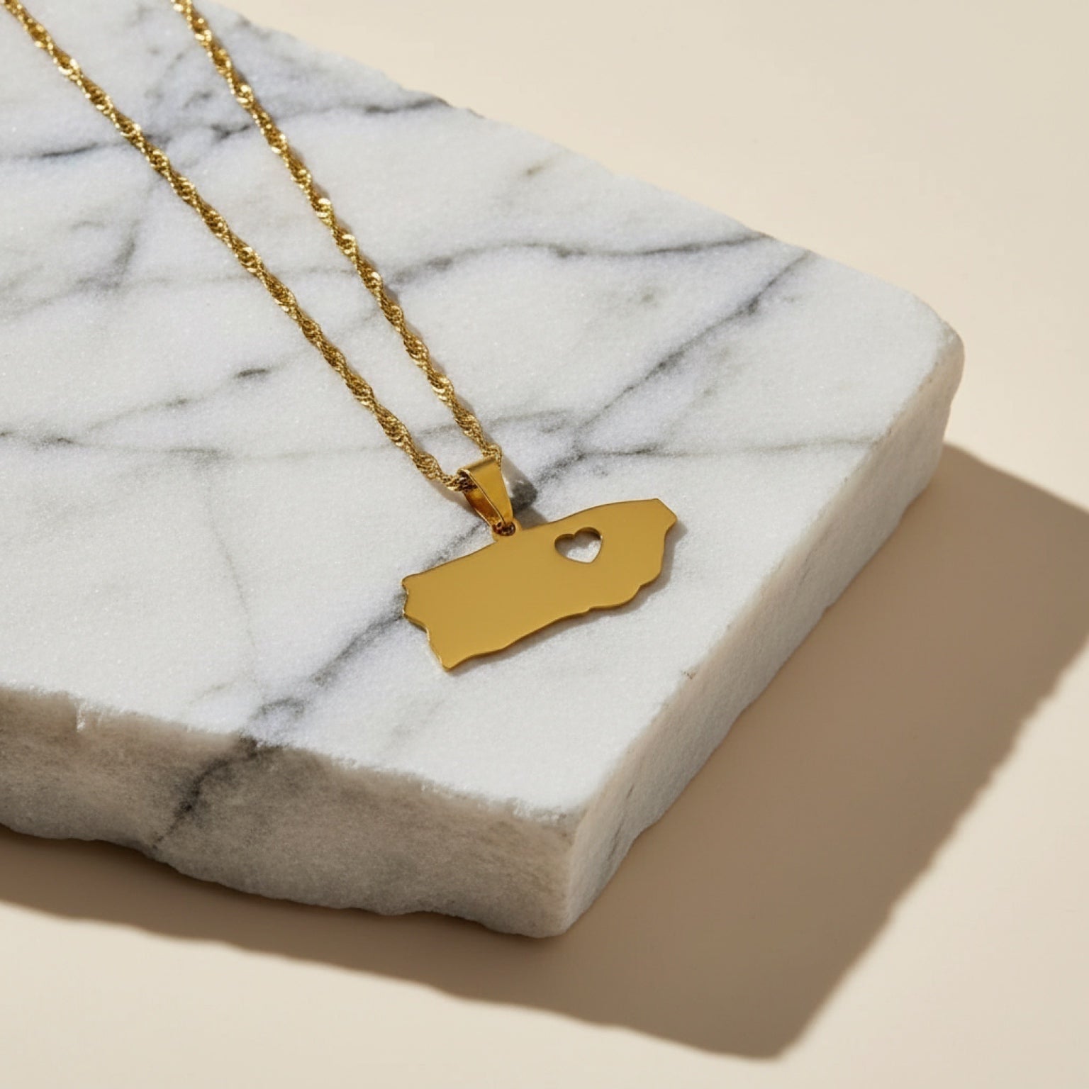 Chévereh gold-tone stainless steel island pendant necklace with heart cutout on a marble surface.