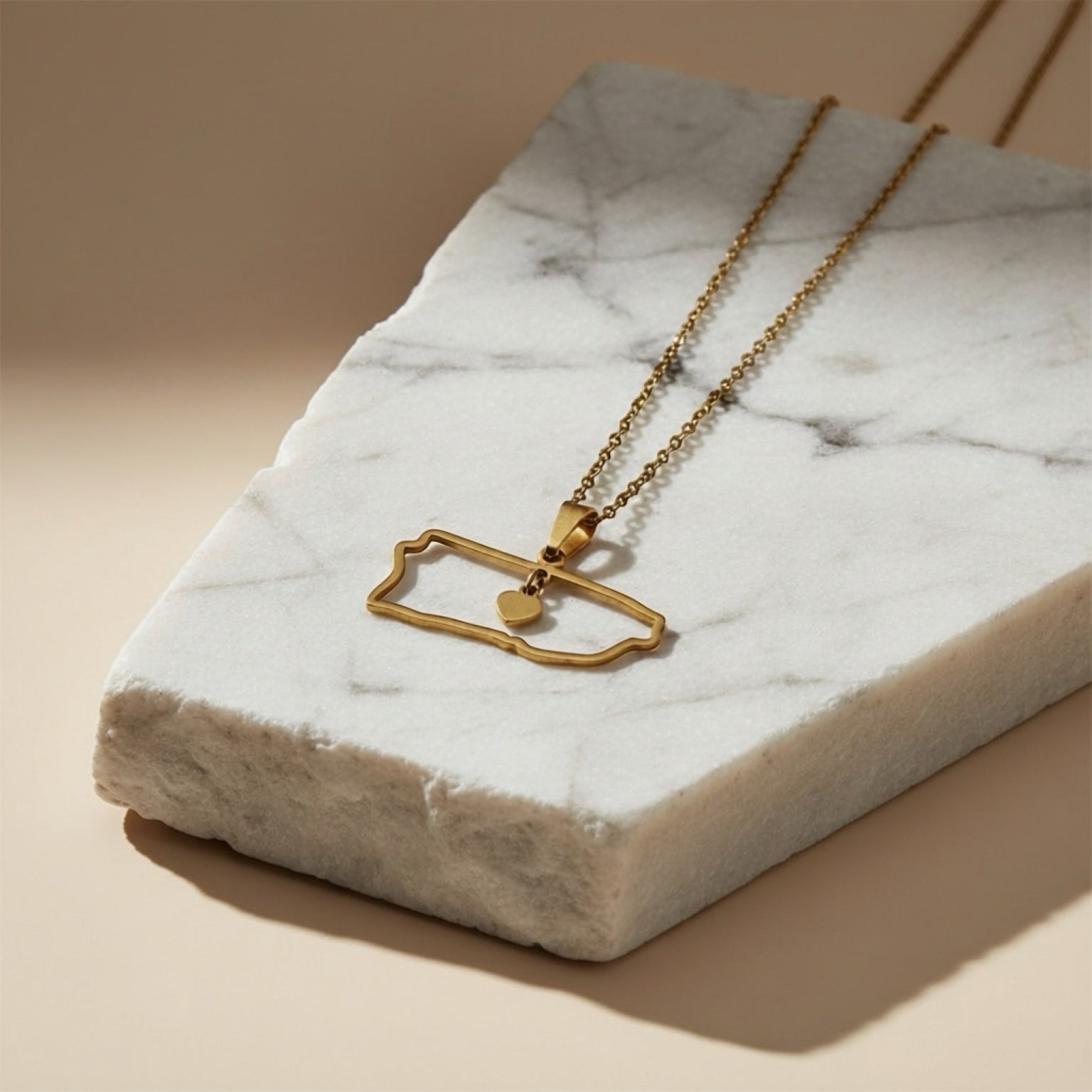 Chévereh gold-tone metal island outline pendant necklace with a small dangling heart charm.