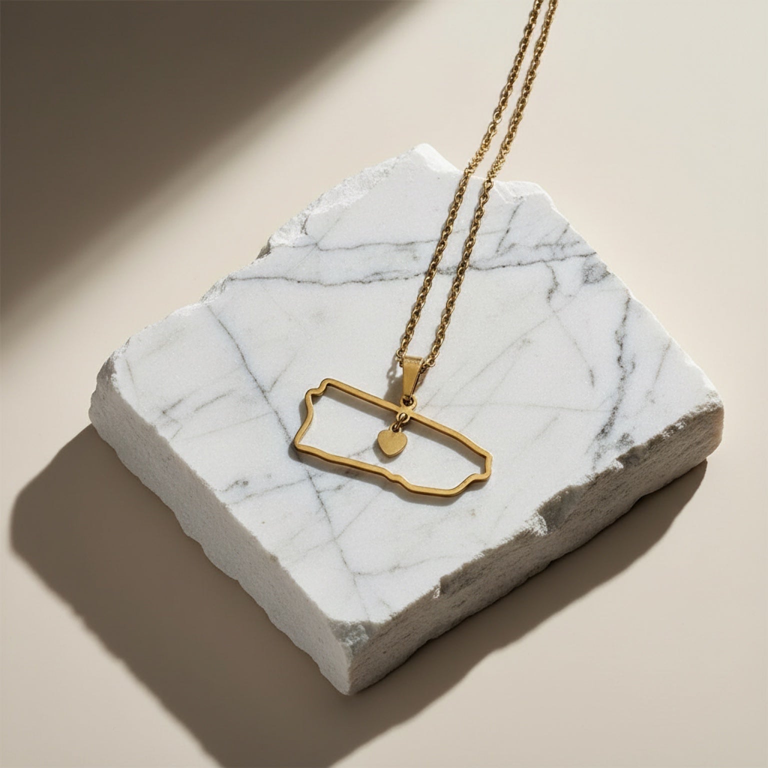 Chévereh gold-tone metal island outline pendant necklace with a small dangling heart charm.