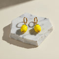 Chévereh gold hoop earrings with glossy yellow glass lemon charms and green leaf details on a marble display