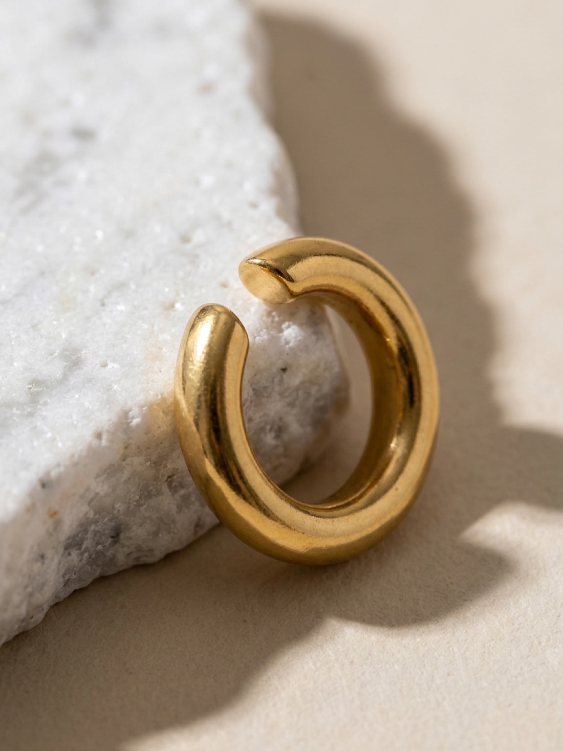 Chévereh minimalist gold ear cuff with a smooth polished finish resting on a textured white stone surface