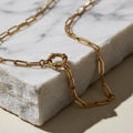 Chévereh gold-tone stainless steel paperclip chain necklace with a stylish sailor clasp on a white marble block.
