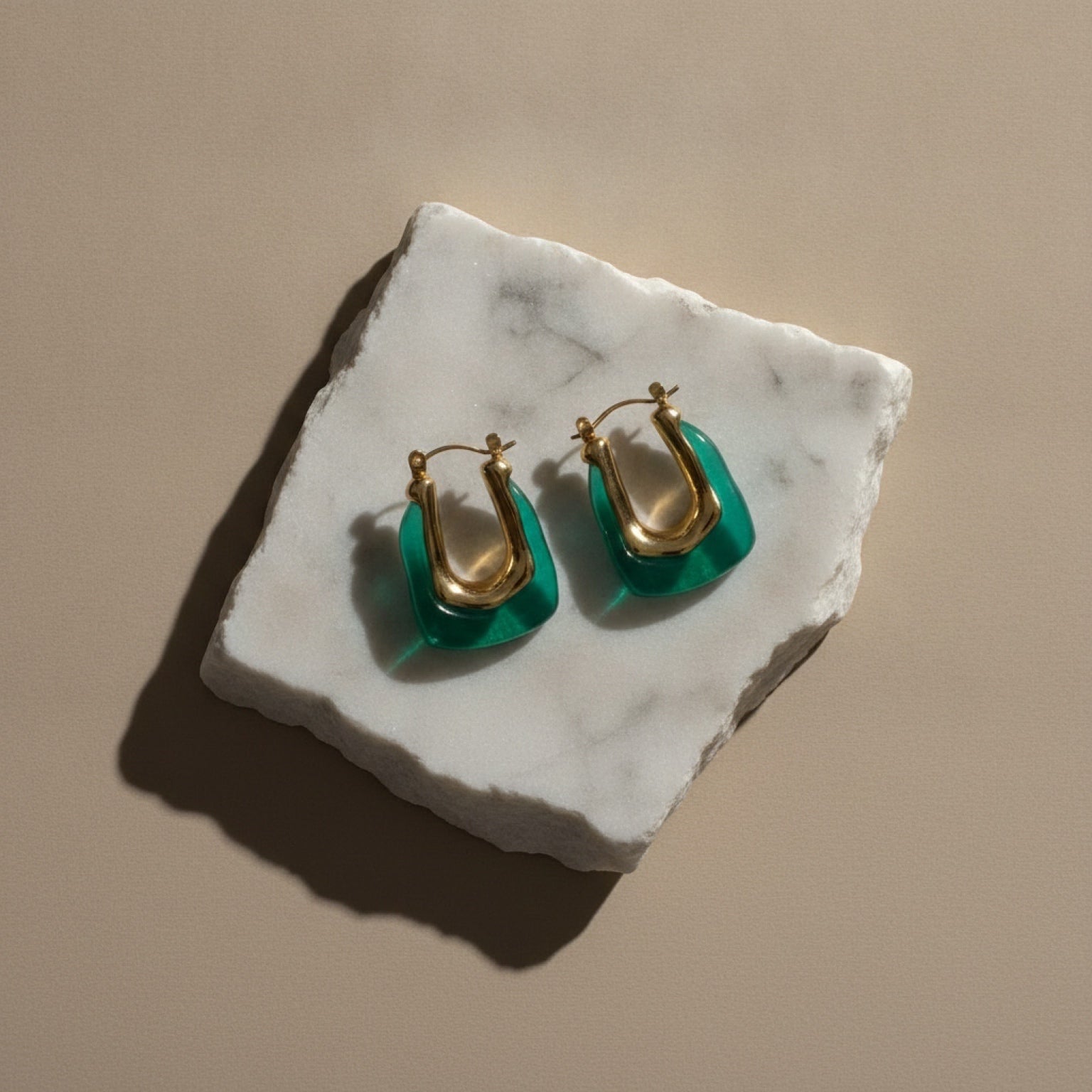Chévereh sculptural hoop earrings featuring gold-tone stainless steel and translucent emerald green resin on marble.