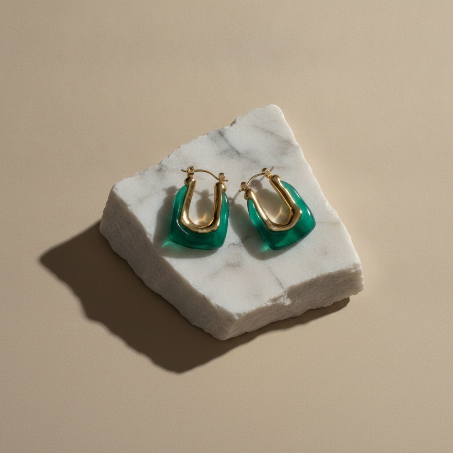 Chévereh sculptural hoop earrings featuring gold-tone stainless steel and translucent emerald green resin on marble