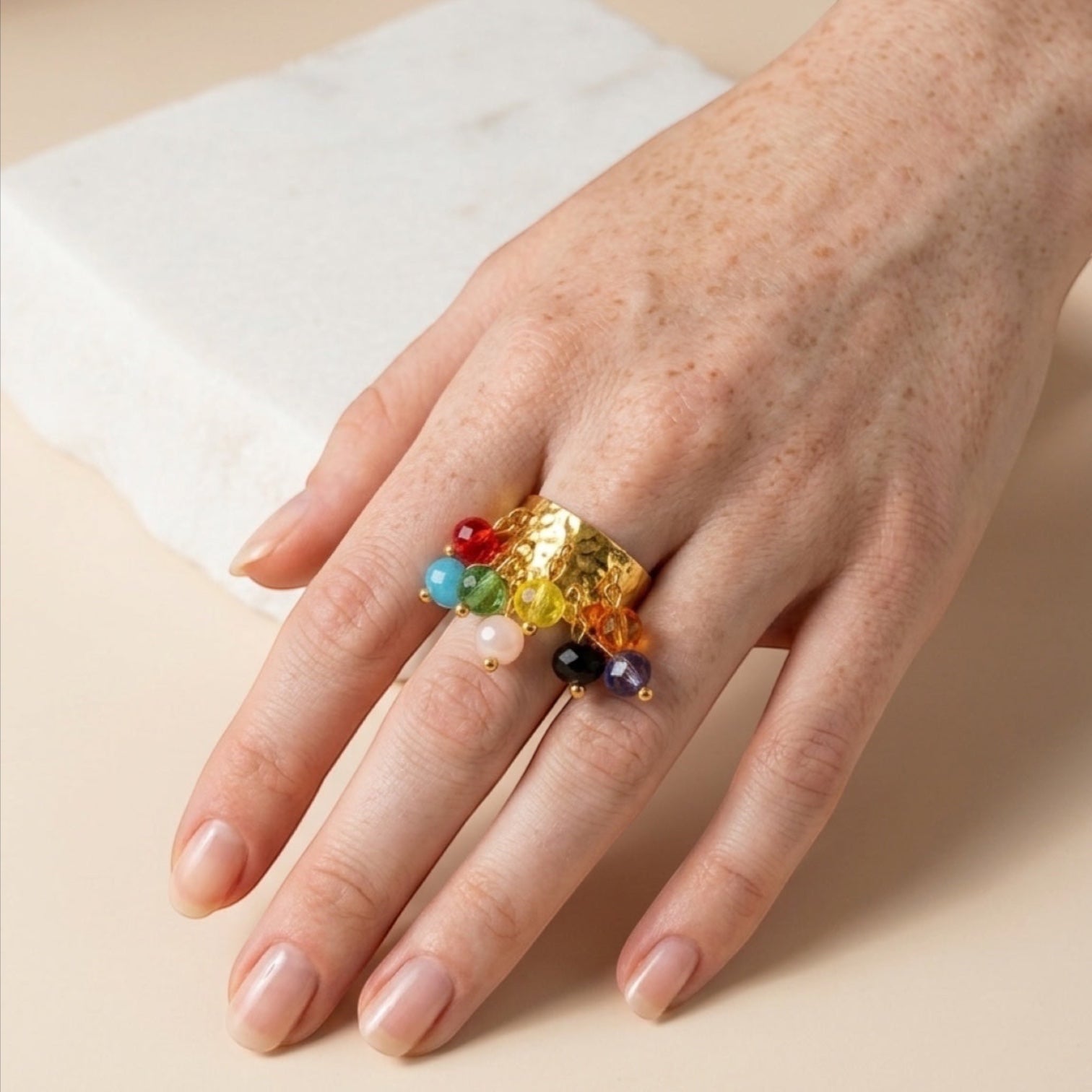 Chévereh gold hammered metal statement ring with dangling multi-colored beaded charms on a hand