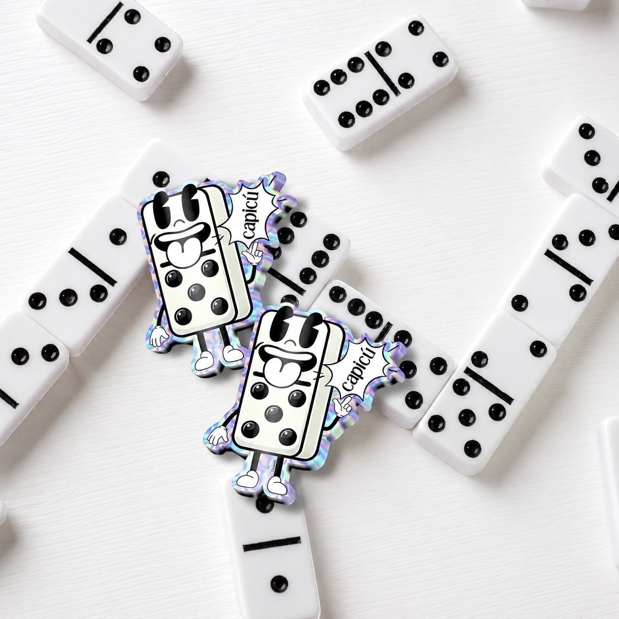 Chévereh holographic Capicú domino sticker with cartoon character and rainbow finish, surrounded by white dominoes.