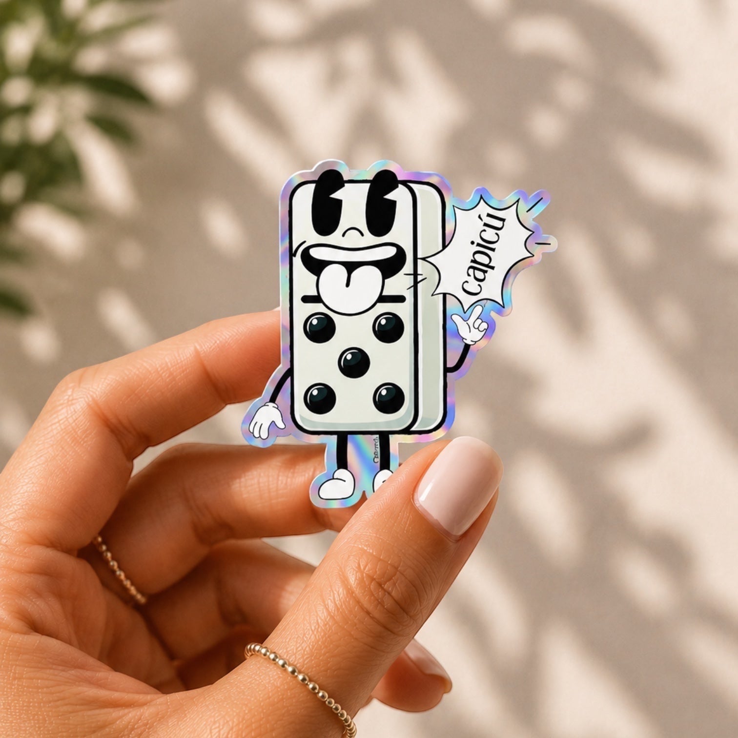 Chévereh holographic vinyl sticker of a cartoon domino character with a tongue sticking out and the word Capicú in a speech bubble.