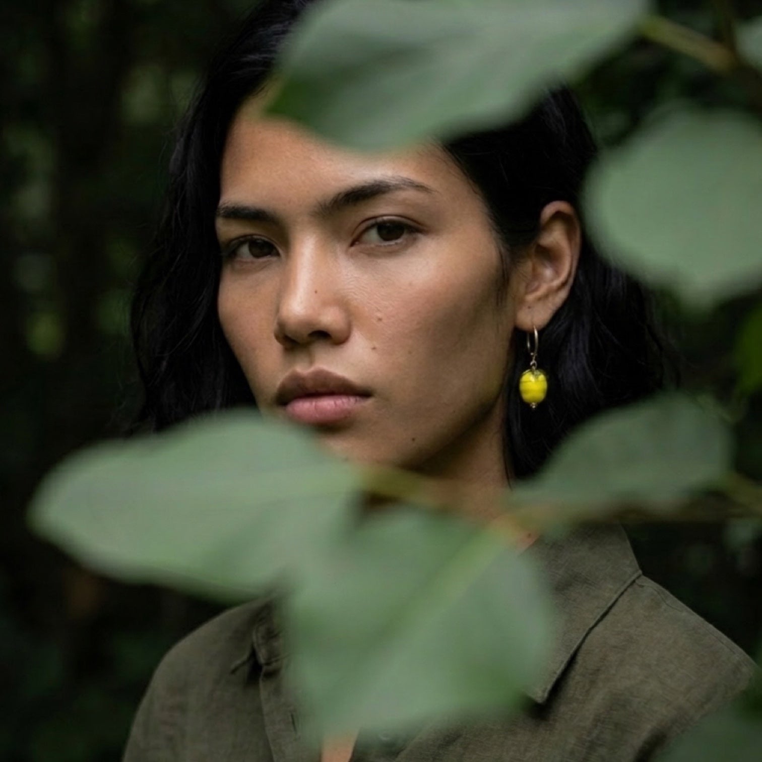 Chévereh gold hoop earrings with glossy yellow lemon charms and green leaves worn by a woman in a forest setting