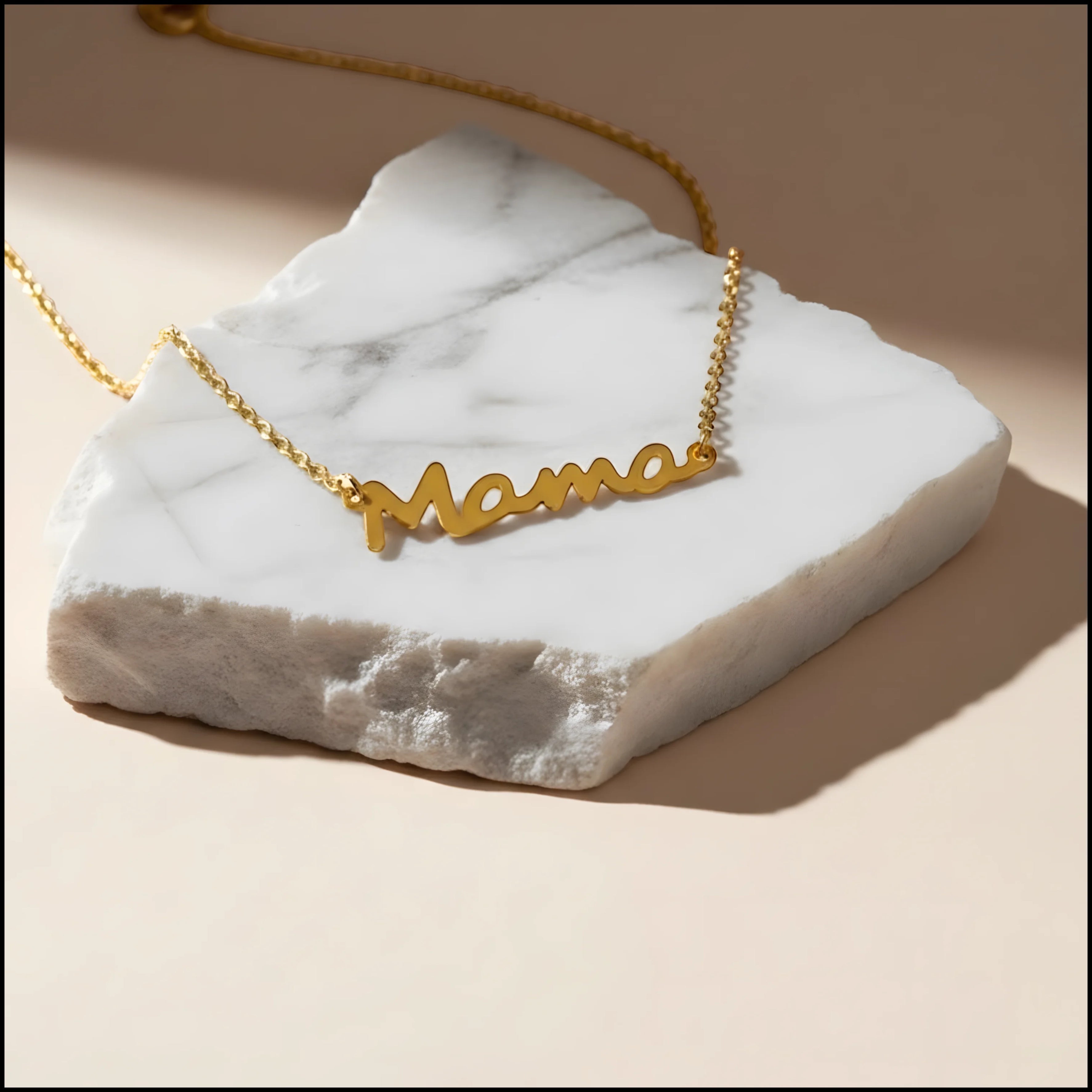 Chévereh gold tone stainless steel Mama script pendant necklace resting on a white marble stone.