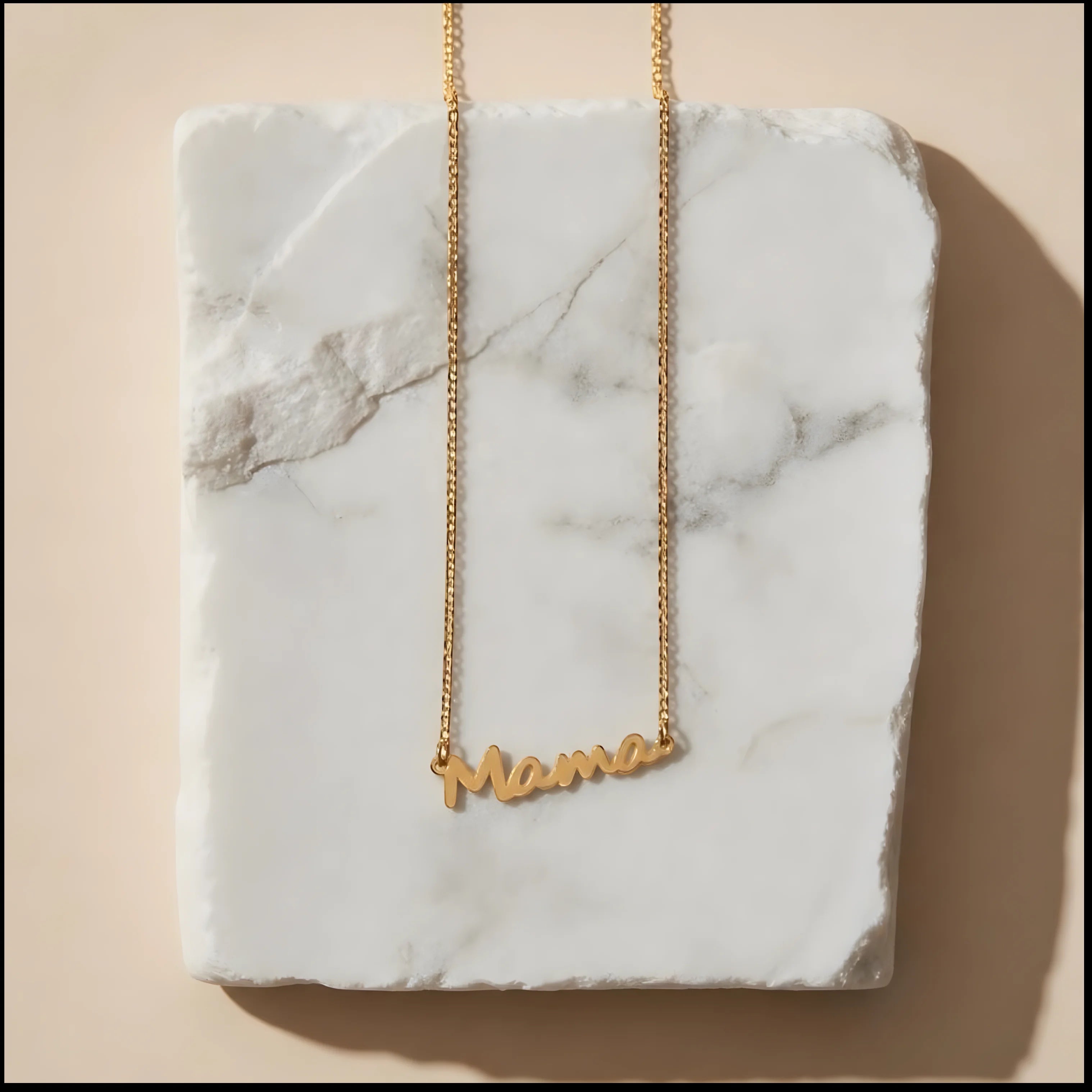 Chévereh gold-tone stainless steel Mama script pendant necklace on a white marble display block.