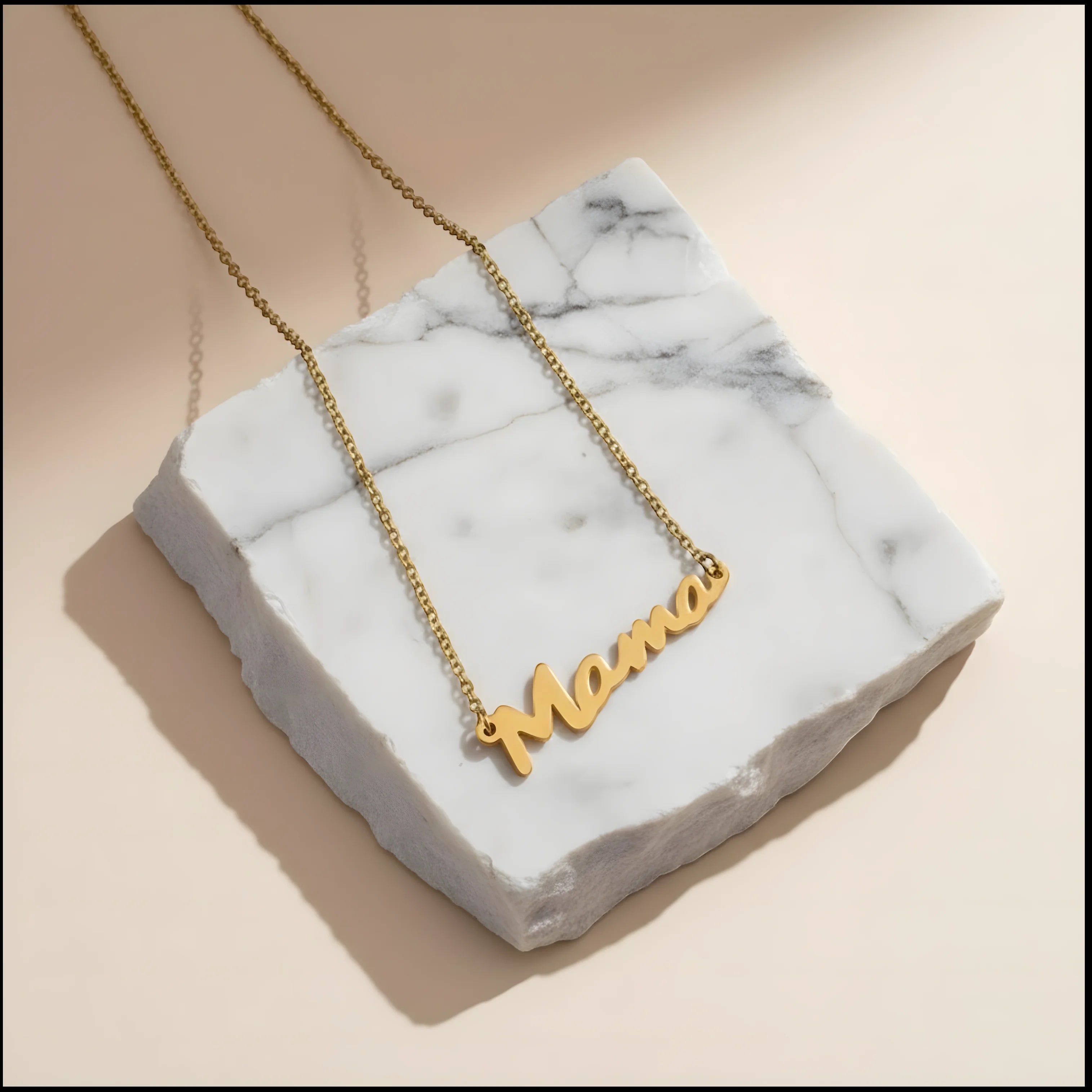 Chévereh gold-tone stainless steel Mama script pendant necklace on a white marble display block.