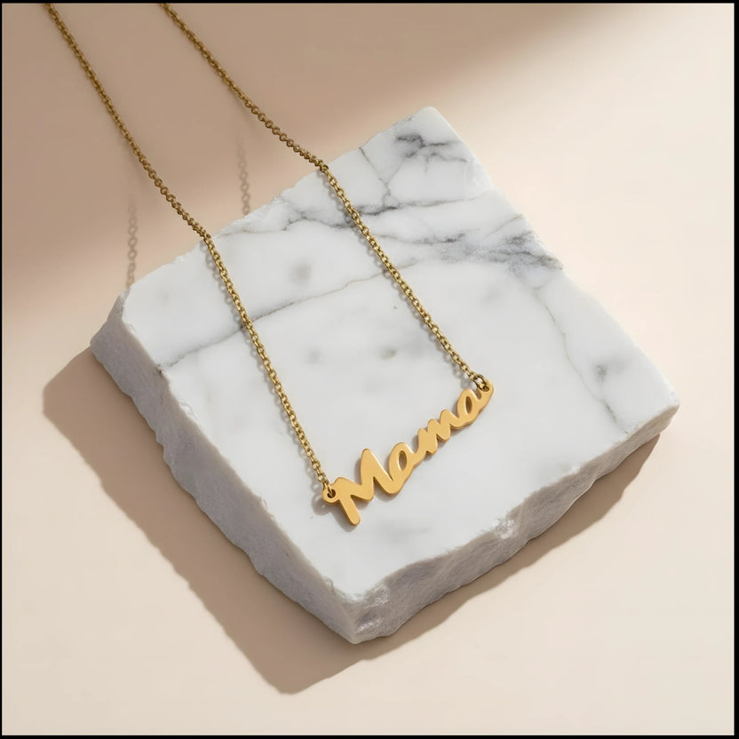 Chévereh gold-tone stainless steel Mama script pendant necklace on a white marble display block.