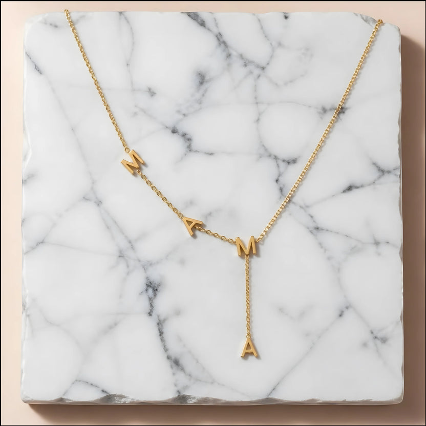 Chévereh gold-tone stainless steel Y-necklace featuring MAMA block letter pendants on a white marble background.