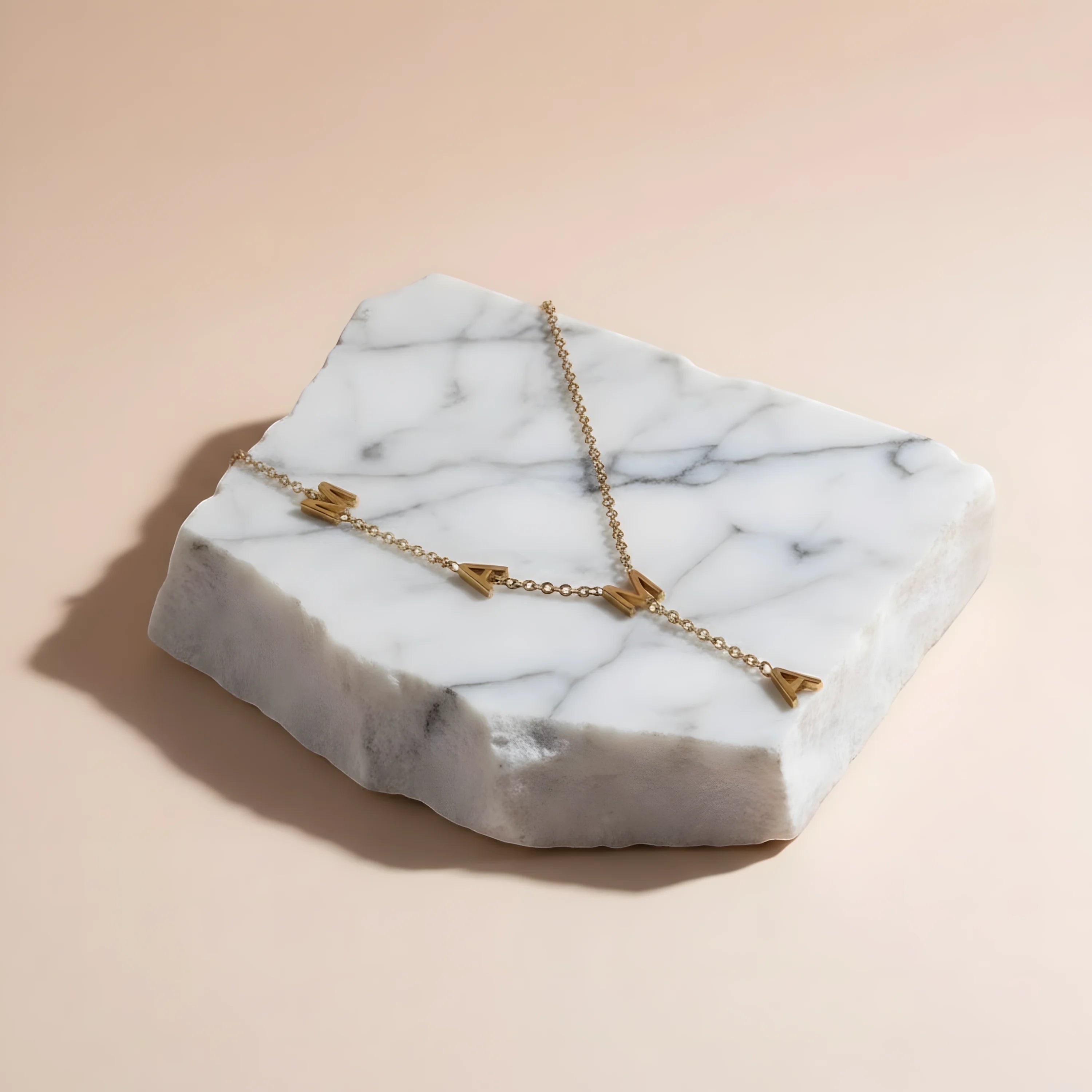 Chévereh gold-tone stainless steel Mama Y necklace with block letter pendants displayed on a white marble stone.