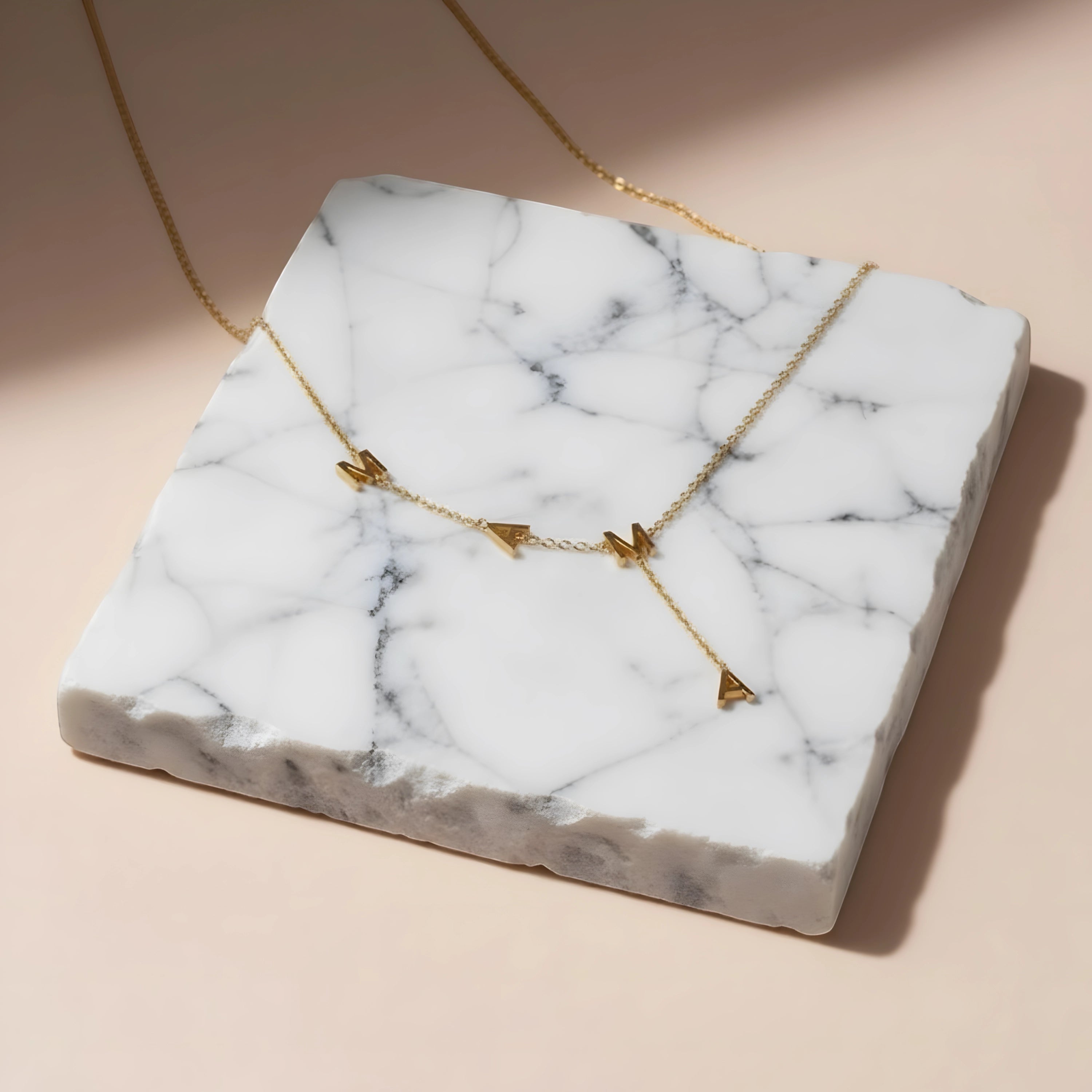 Chévereh gold-tone stainless steel Mama Y-drop necklace with block letter pendants displayed on a marble slab.