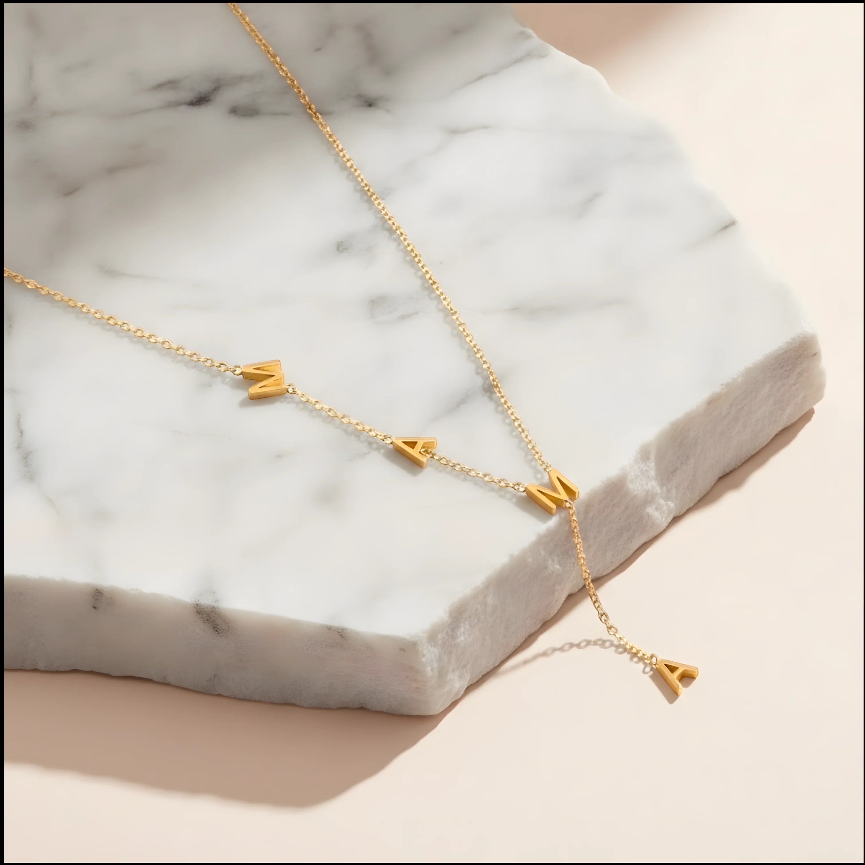 Chévereh gold-tone stainless steel Y-necklace featuring MAMA block letter pendants on a marble display.