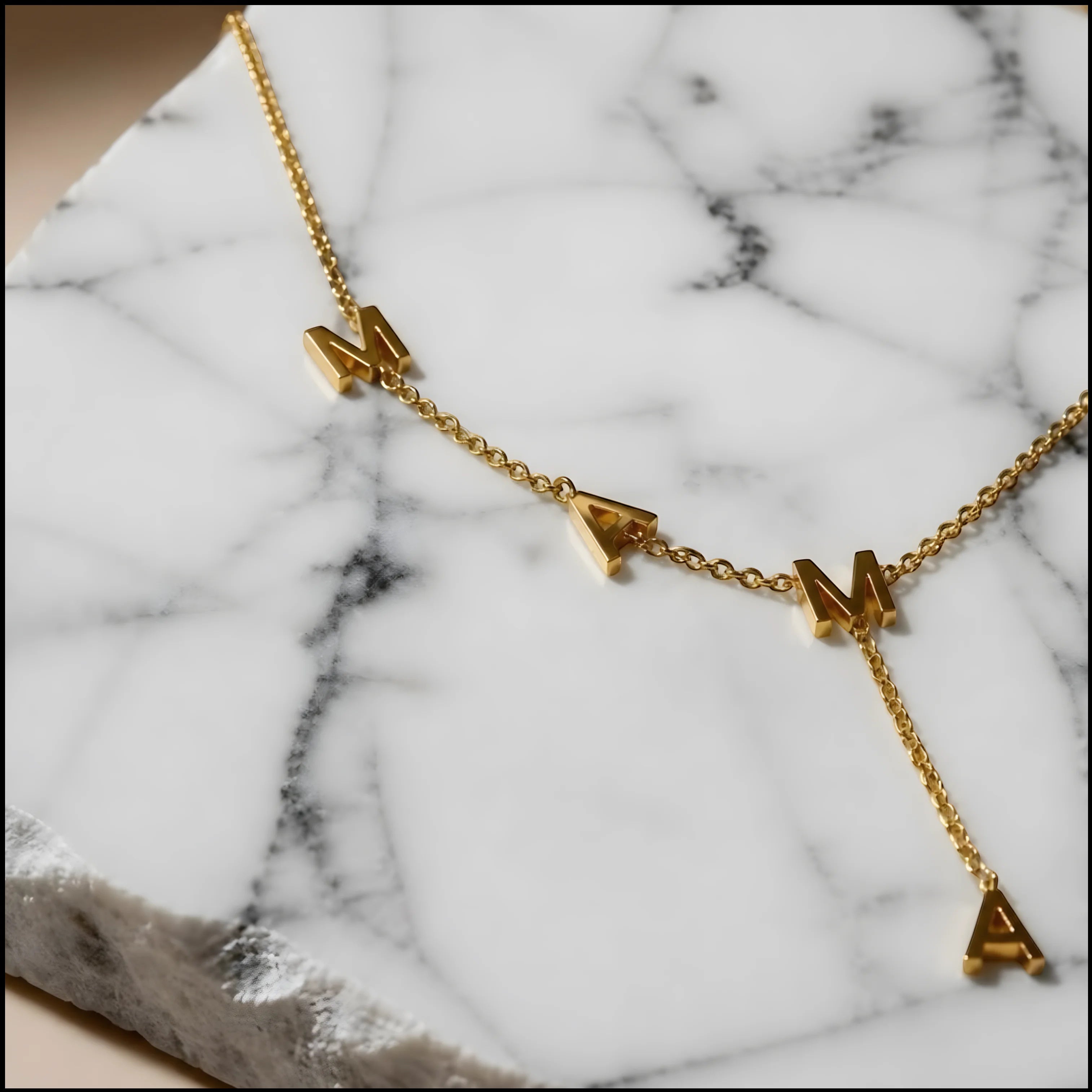 Chévereh gold-tone stainless steel Y-necklace featuring MAMA block letter pendants on a marble display.
