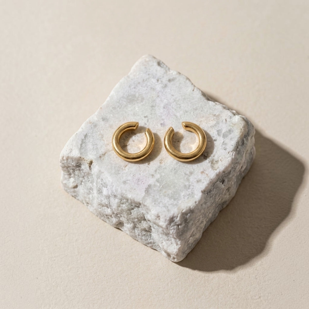 Chévereh minimalist gold ear cuffs with a smooth polished finish resting on a textured white stone block