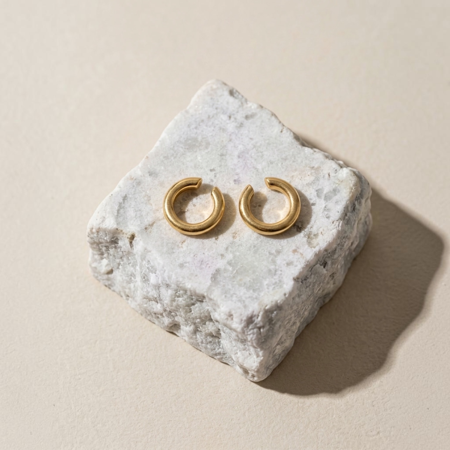 Chévereh minimalist gold ear cuffs with a smooth polished finish resting on a textured white stone block
