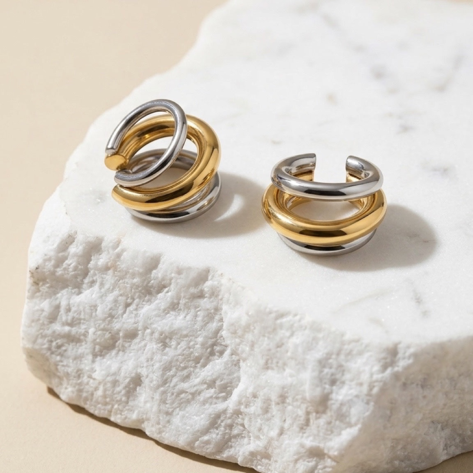 Chévereh minimalist gold and silver layered ear cuffs resting on a textured white stone block.