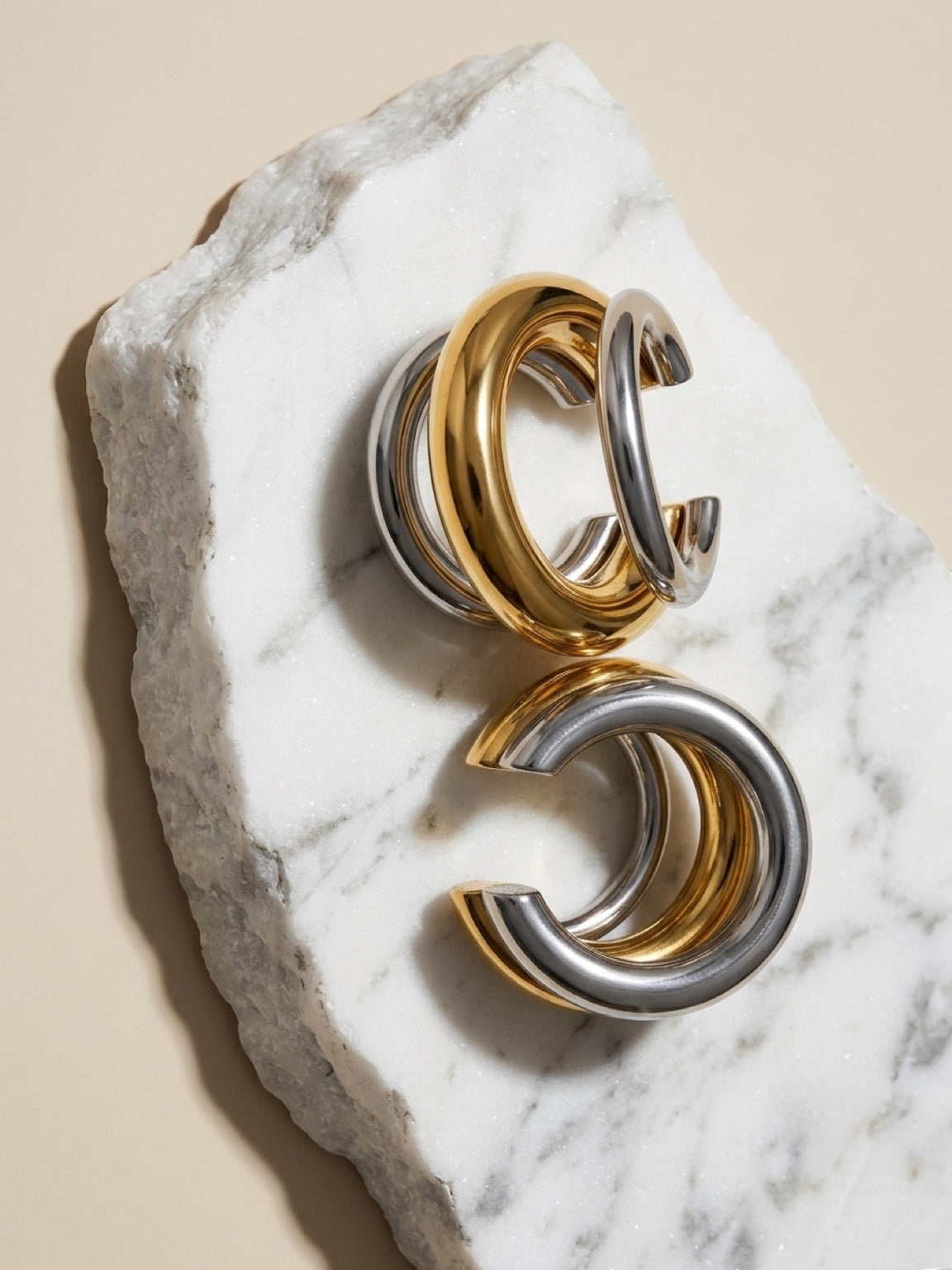 Chévereh minimalist ear cuffs in polished gold and silver tones, stacked on a white marble surface.
