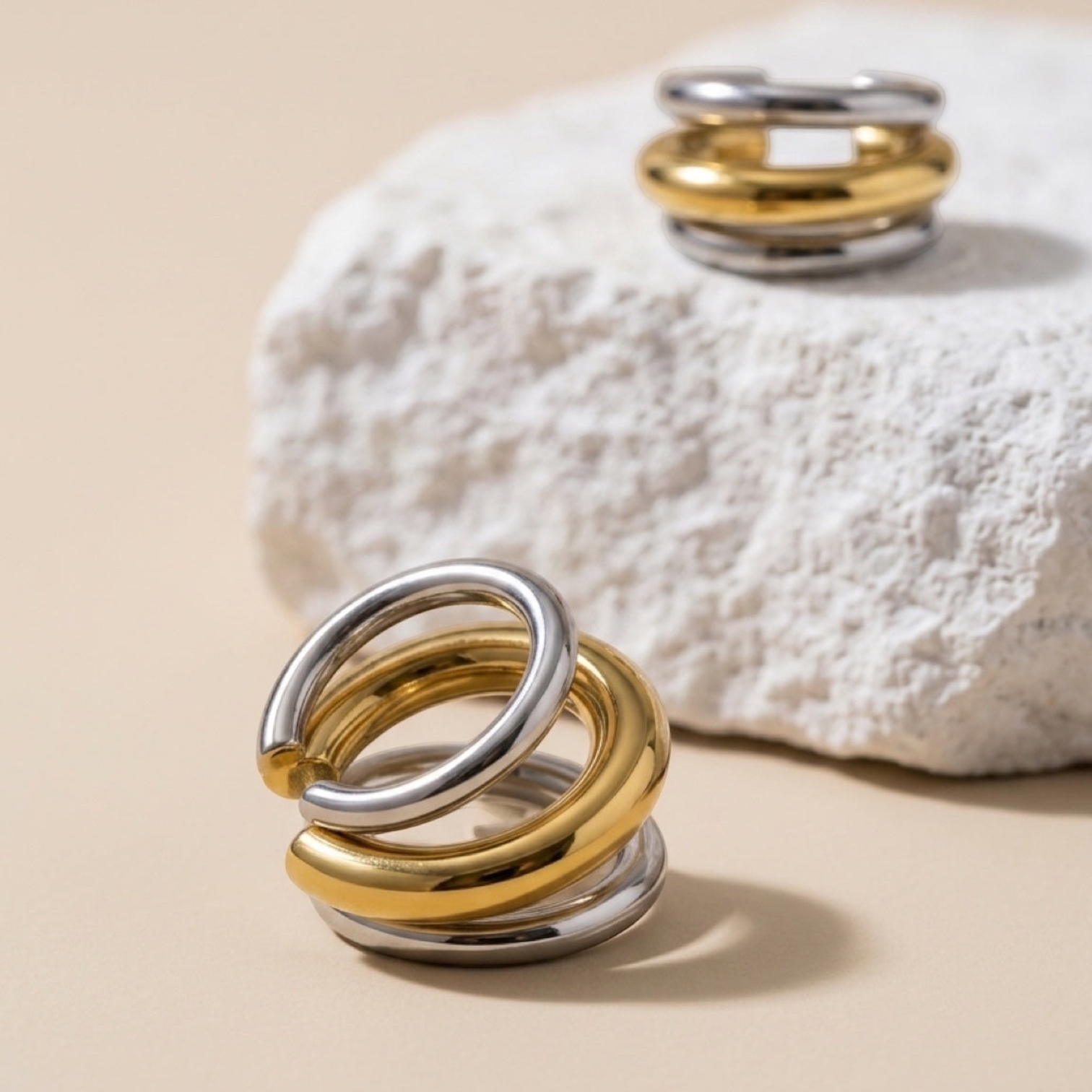 Chévereh minimalist ear cuffs in polished gold and silver tones stacked on a textured white stone surface.