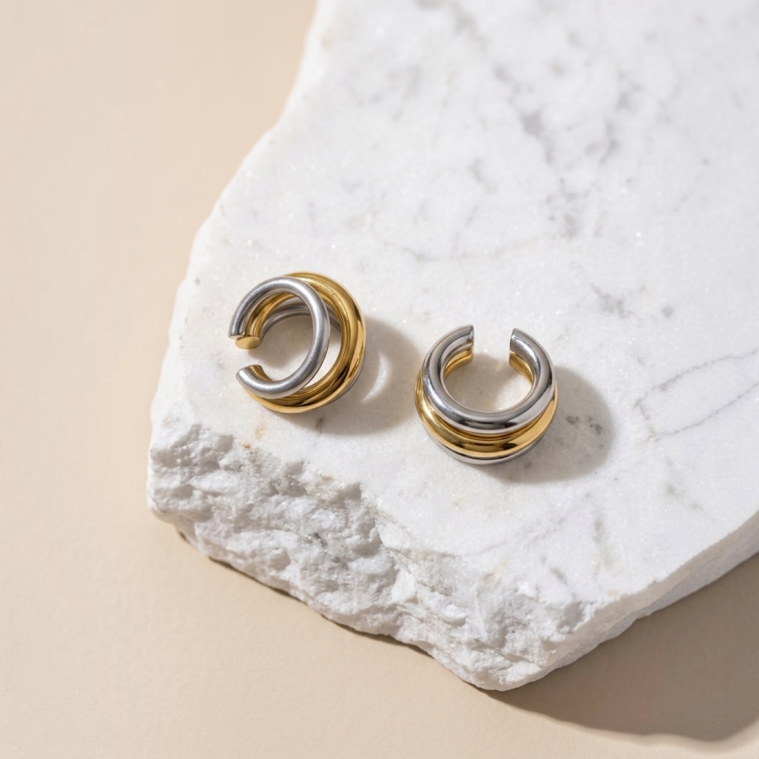 Chévereh minimalist gold and silver layered ear cuffs resting on a textured white marble stone surface.