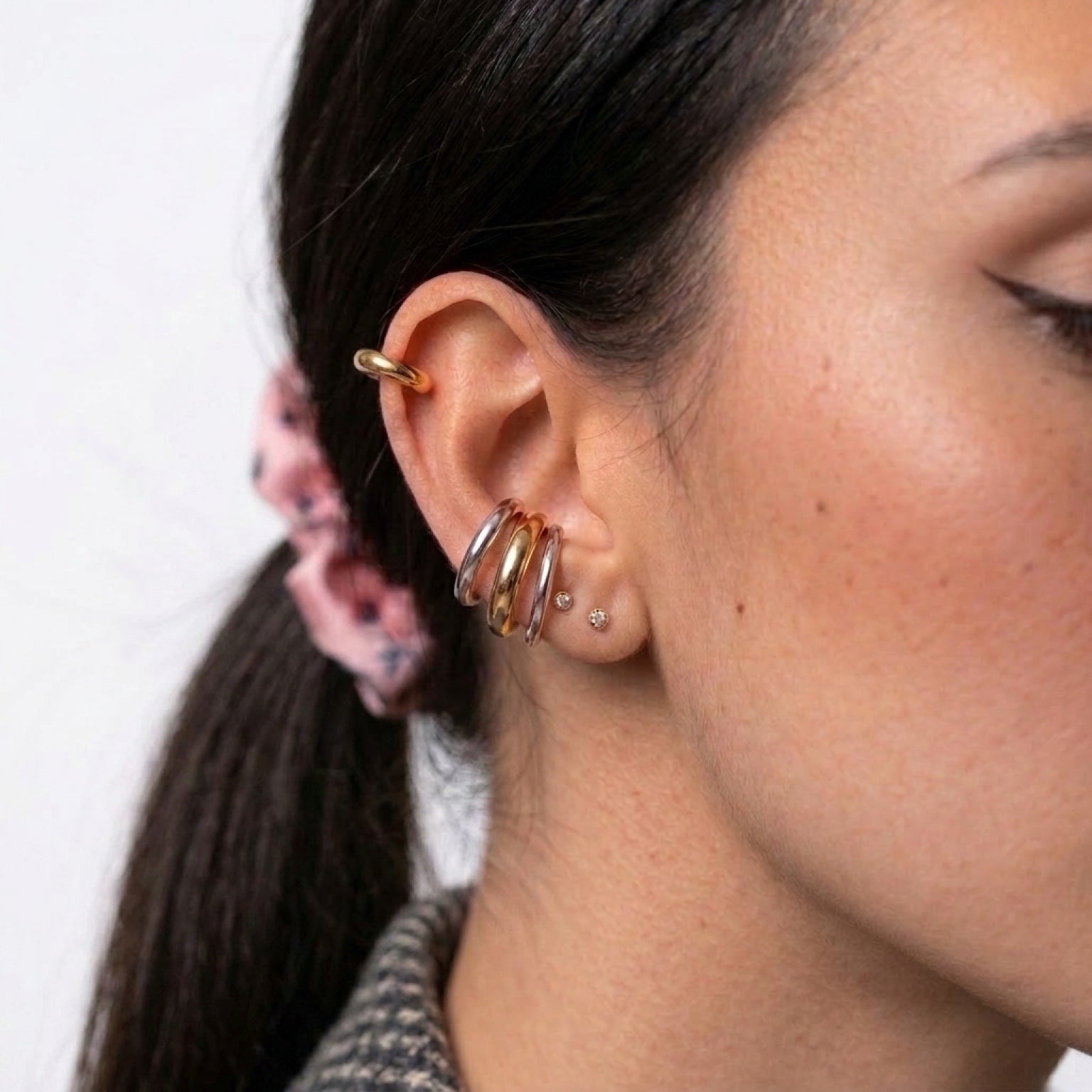Chévereh minimalist ear cuffs in gold and silver tones stacked on a model's ear for a modern layered look.