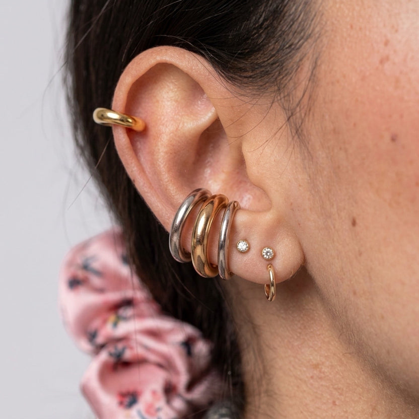 Chévereh minimalist gold and silver ear cuffs stacked on a model's ear, featuring polished open-hoop designs.