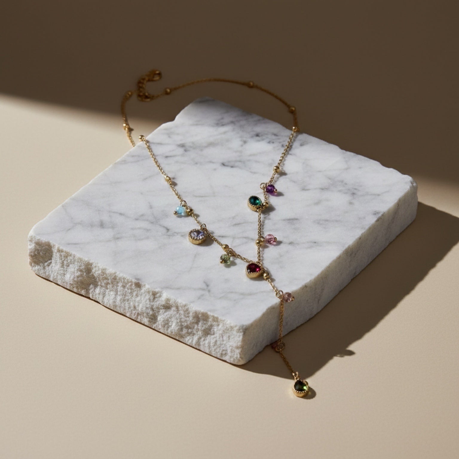 Chévereh dainty gold-tone stainless steel drop necklace with colorful multifaceted stones on a marble display block.