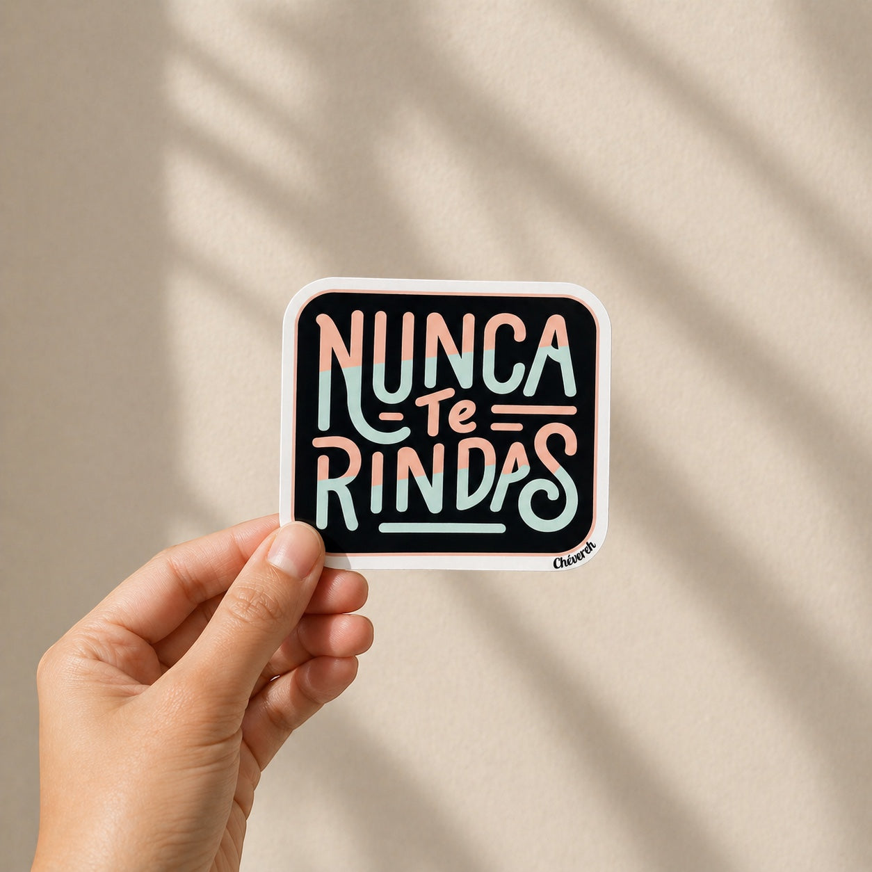 Chévereh "Nunca Te Rindas" vinyl sticker with pastel lettering on a black background. Waterproof and glossy finish.