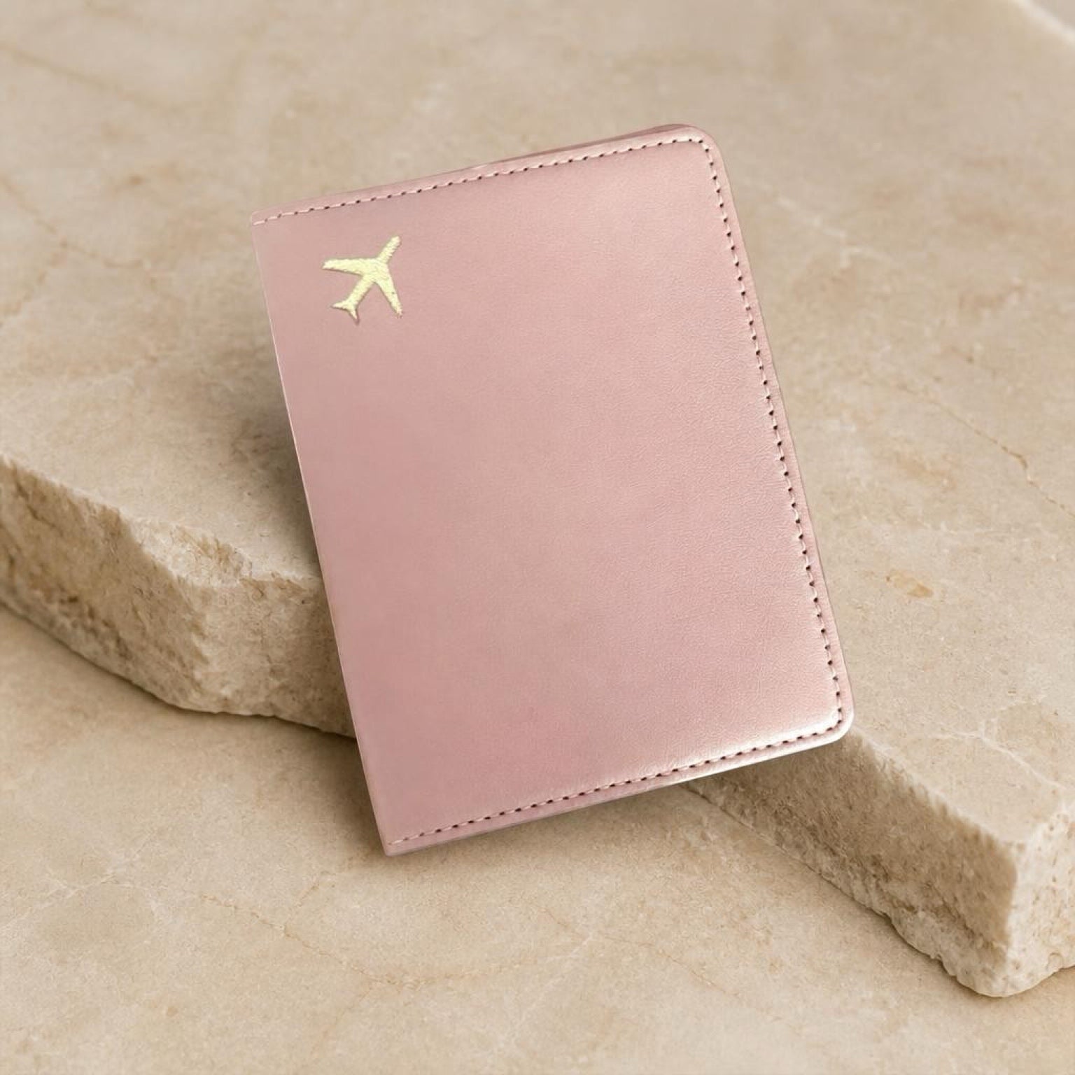 Chévereh pink PU leather passport holder with a minimalist gold airplane emblem on a textured stone surface.