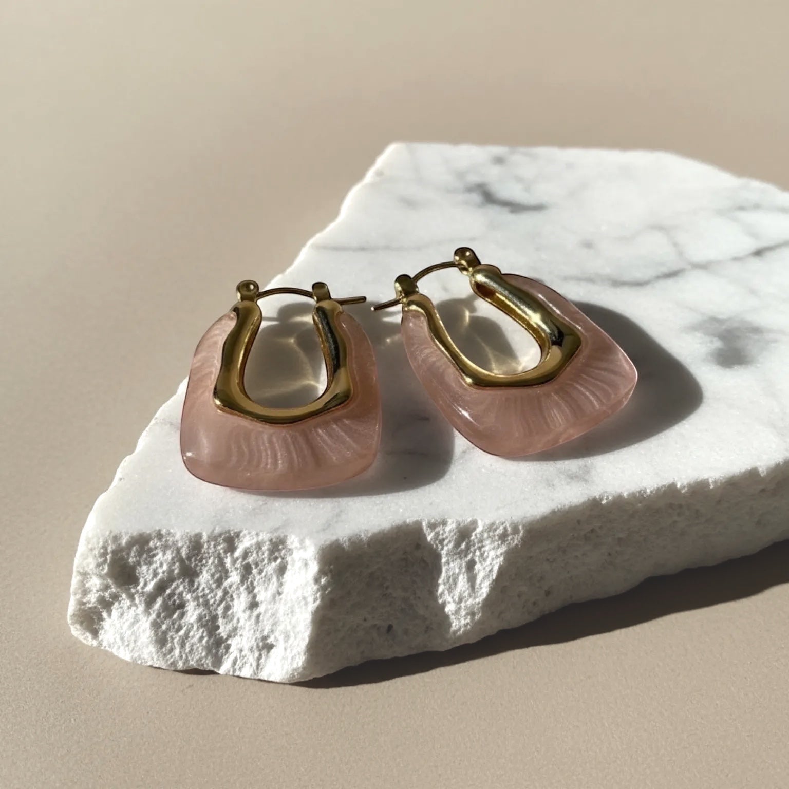 Chévereh blush pink resin and gold sculptural hoop earrings with a translucent finish and unique texture.