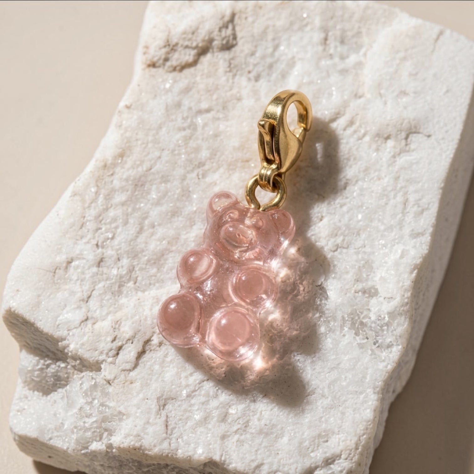 Chévereh translucent pink resin gummy bear charm with a polished 14K gold-plated lobster clasp on a textured stone.