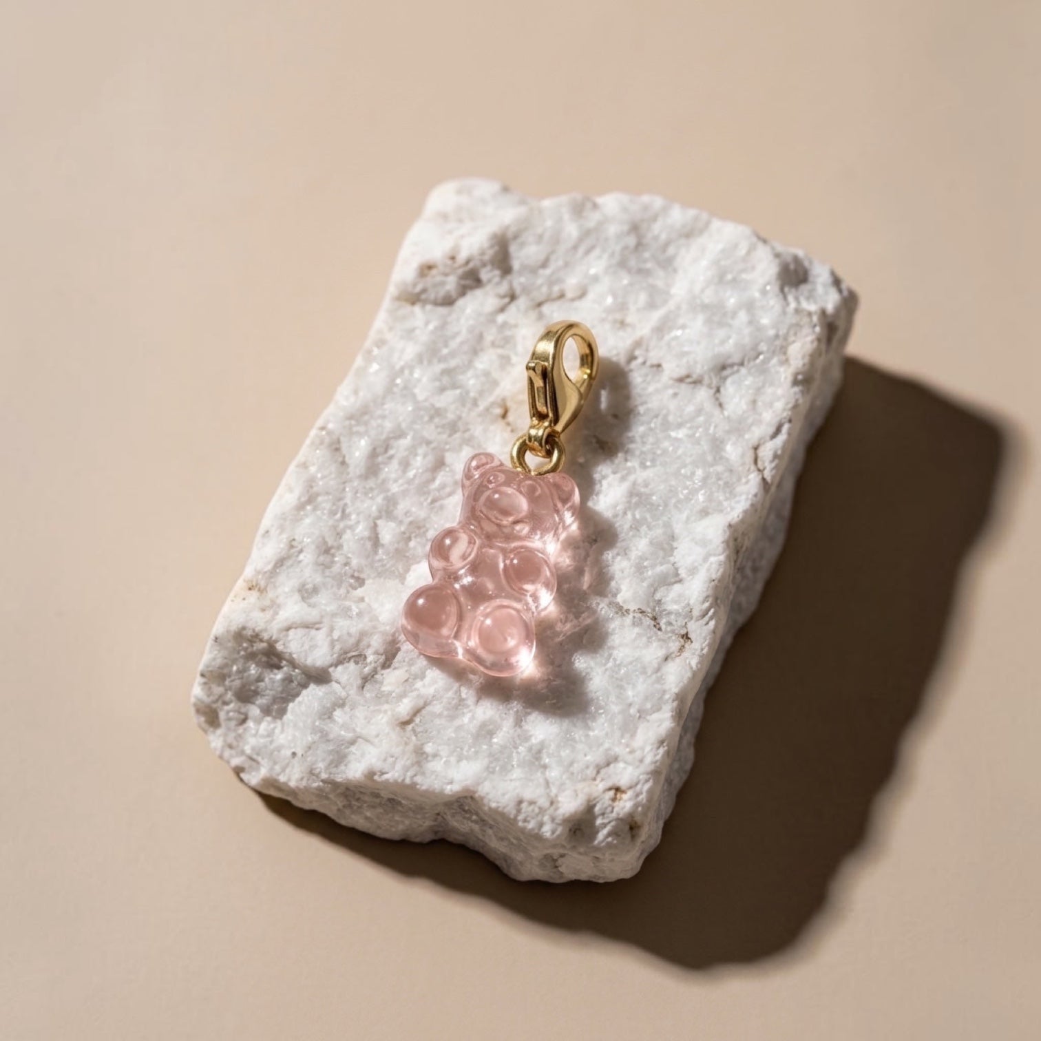 Chévereh translucent pink resin gummy bear charm with a 14K gold-plated lobster clasp resting on a white stone.