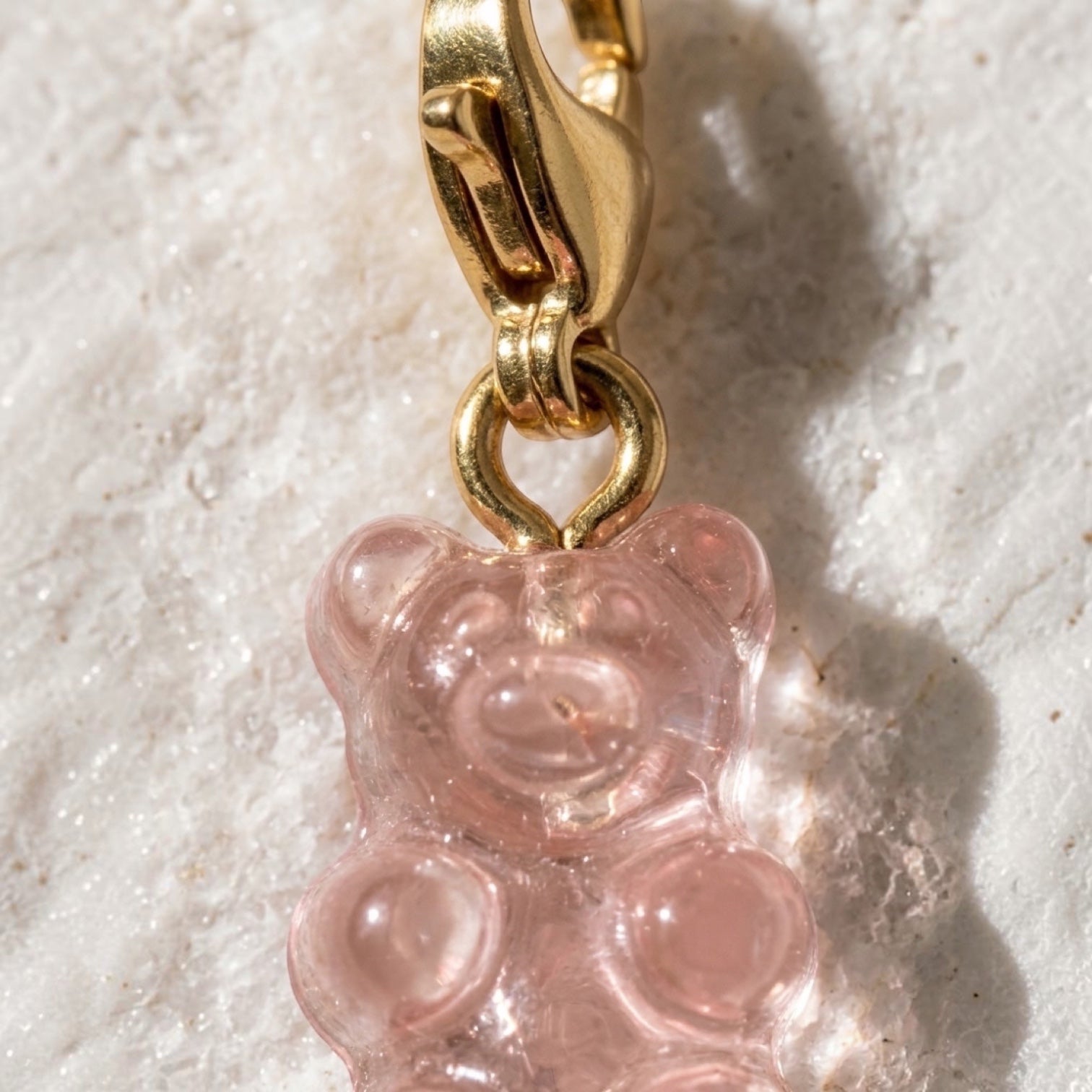 Chévereh translucent pink resin gummy bear charm with a polished 14K gold-plated lobster clasp on a textured surface.