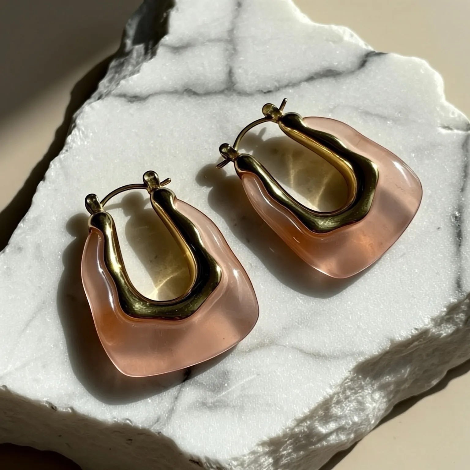 Chévereh sculptural gold-tone and blush-pink resin hoop earrings with a modern, artistic design.