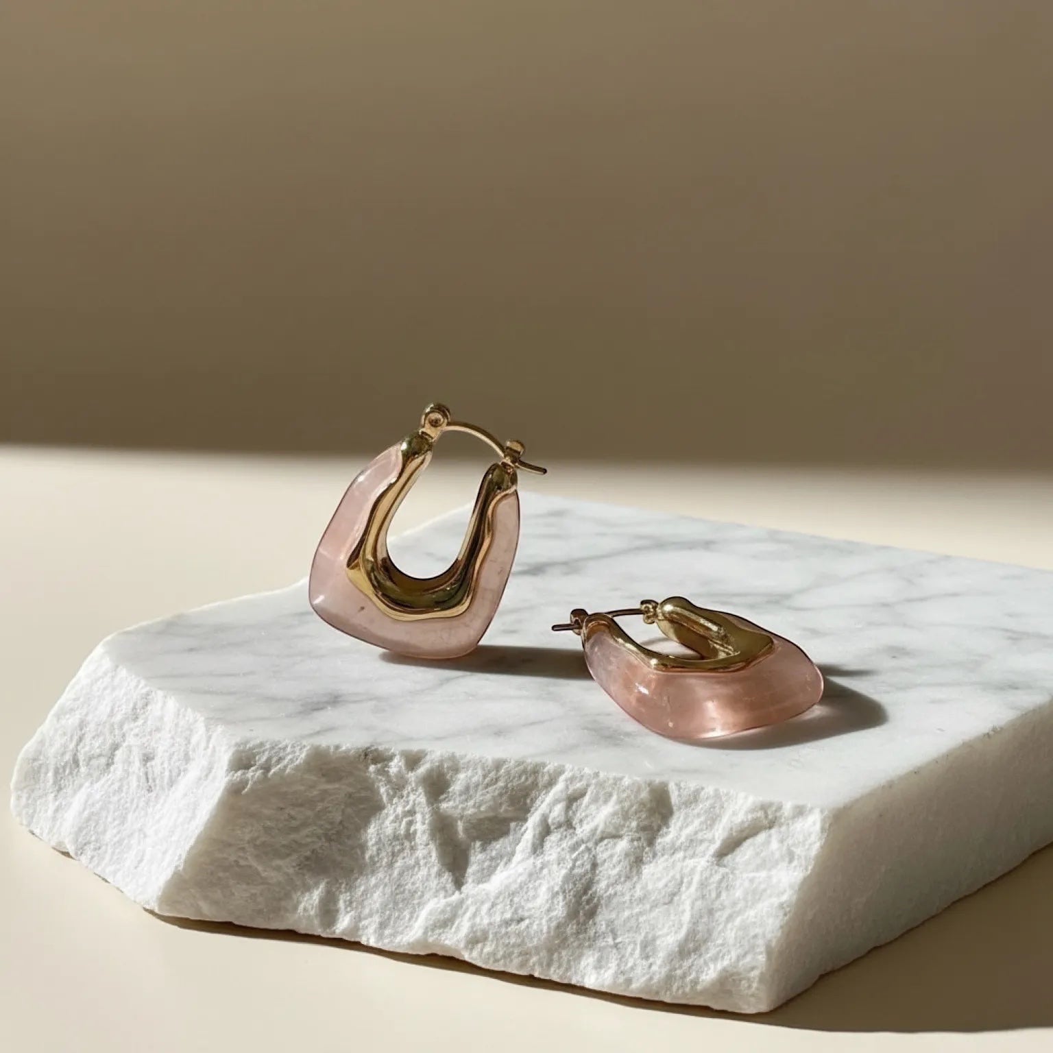 Chévereh Sculptural Resin Hoop Earrings in blush pink resin and gold-tone metal. Modern artistic design.
